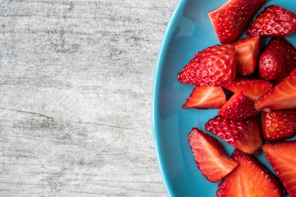 sliced strawberries on a blue plate on a grey counter or table