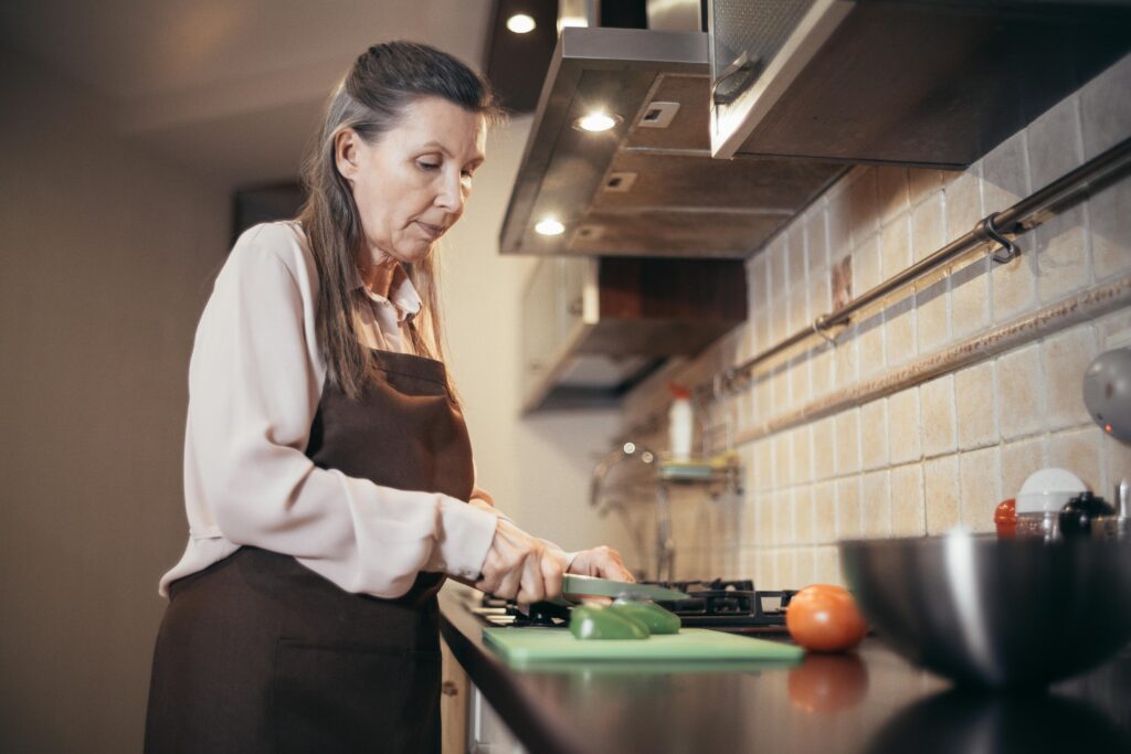 senior woman cooks in kitchen, chops veggies